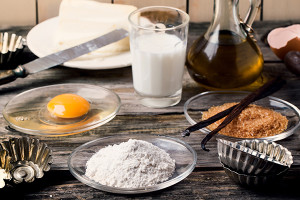 Ingredients for baking (flour, egg, brown sugar, milk) with vintage cupcake's forms on old wooden table